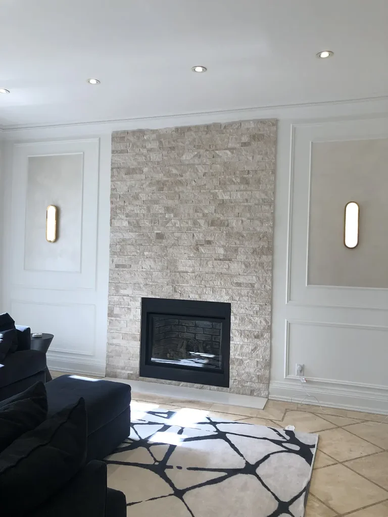 Living room stone fireplace wall lit by flanking wall sconces and recessed pot lights