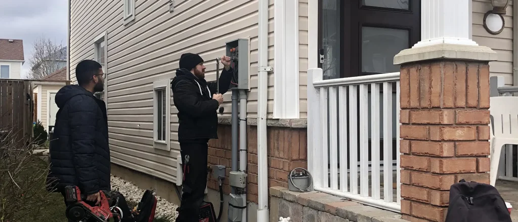 Two electricians talking with a homeowner beside the meter at the side of a house
