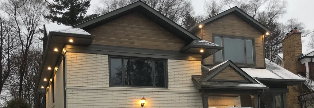 Two-storey home exterior at dusk with lit soffit pot lights and entry lighting