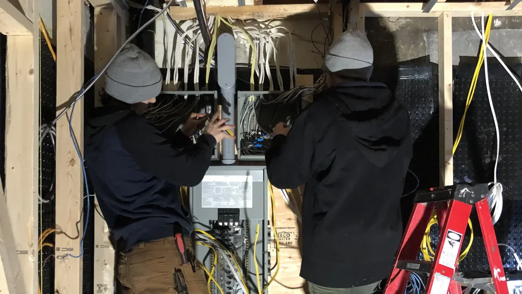 Two electricians working at an open panel during a residential rough-in