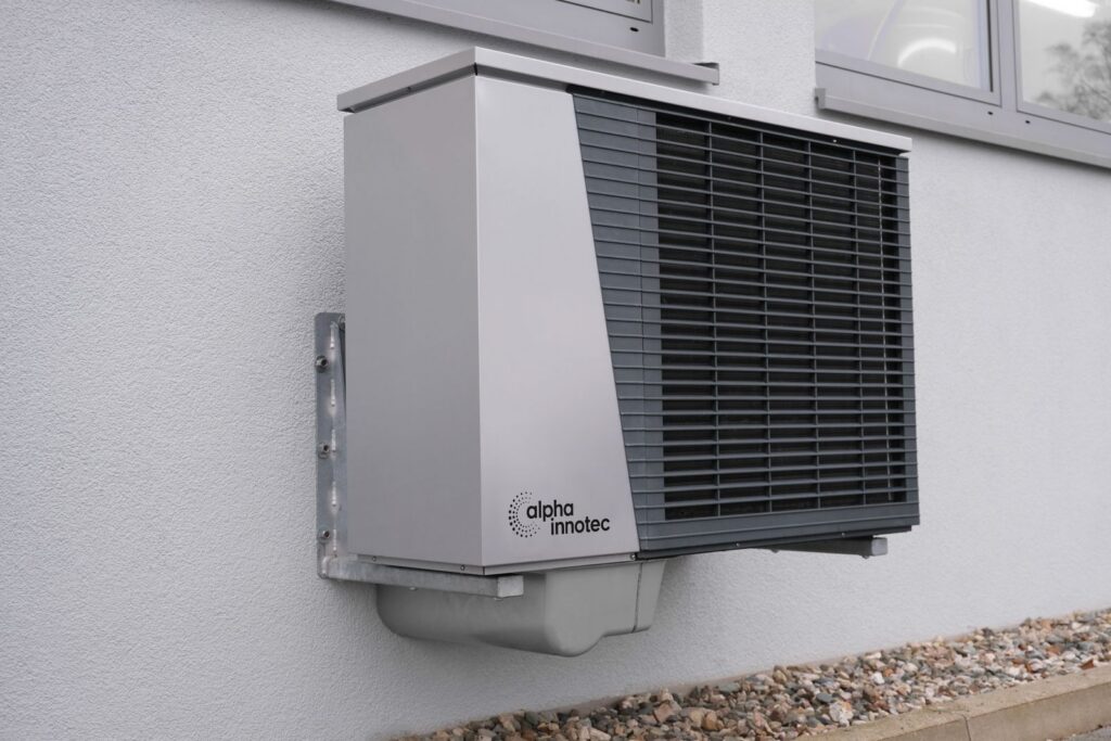 Air-source heat pump outdoor unit mounted on the exterior wall of a house